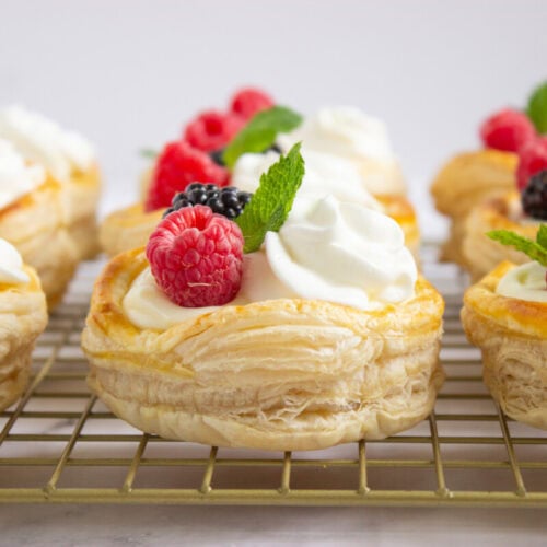 Puff pastry rounds topped with whipped cream, fresh raspberries, blackberries, and mint leaves, arranged on a cooling rack.