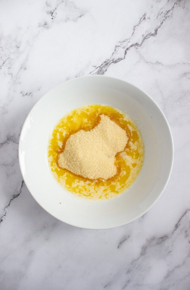 A white bowl containing melted butter and a mound of semolina sits on a marble surface.