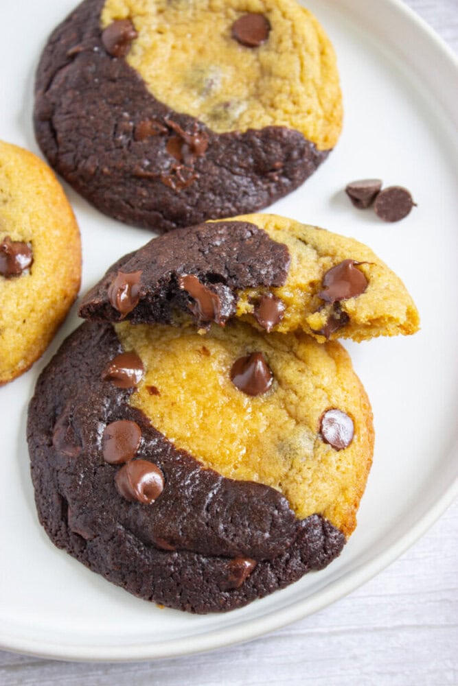 A plate with two half-chocolate, half-vanilla cookies and one broken cookie, all with chocolate chips.
