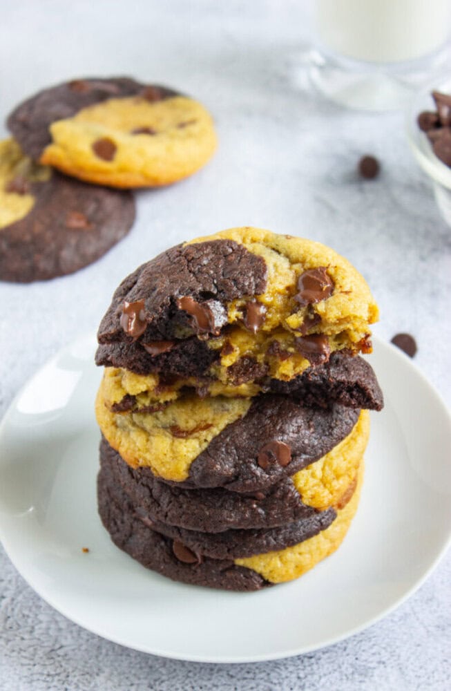 A stack of marbled chocolate and vanilla cookies with chocolate chips on a white plate. One cookie has a bite taken out of it.
