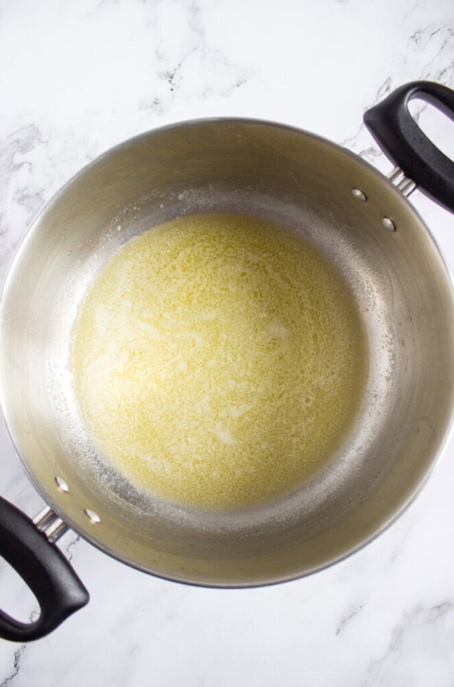 A stainless steel pot with melted butter inside, sitting on a white marble surface.