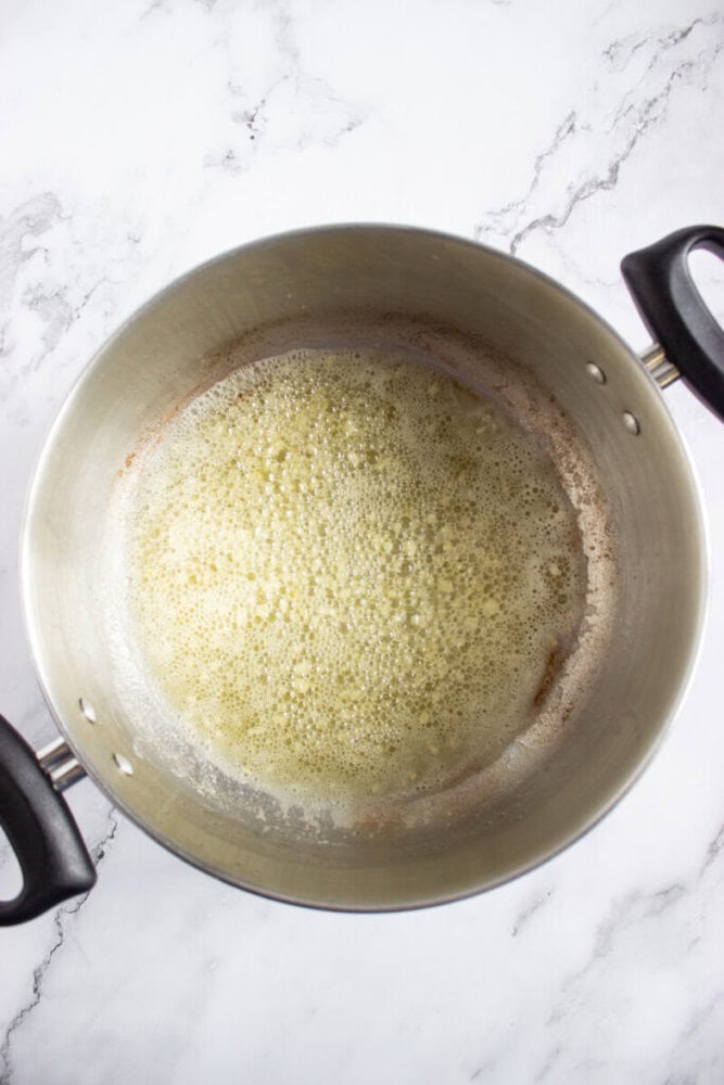 A stainless steel pot with bubbling melted butter on a white marble surface.