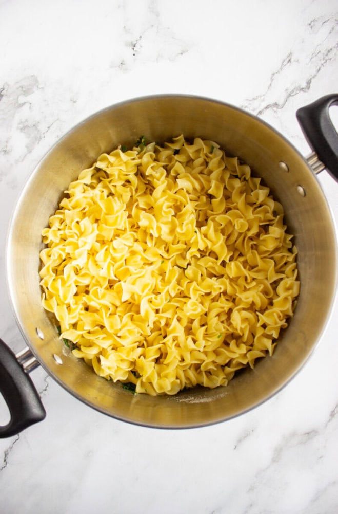 A large pot filled with cooked egg noodles on a marble countertop, viewed from above.