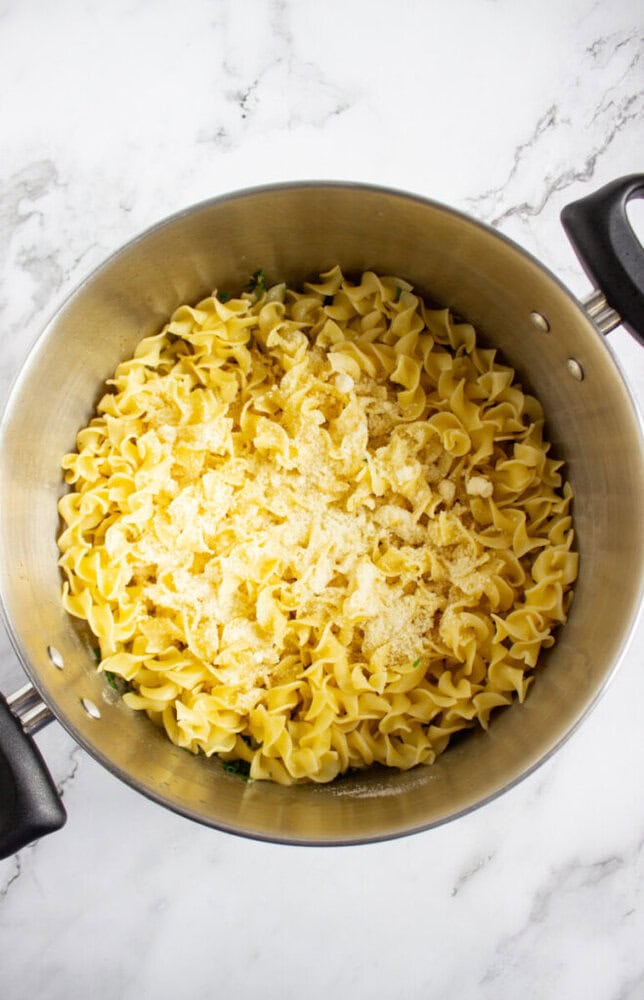 A large pot filled with uncooked egg noodles and powdered seasoning on a marble countertop.
