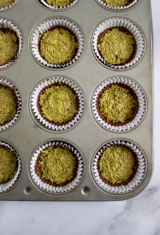 A muffin tin filled with nine baked green muffins in white paper liners, viewed from above on a white surface.