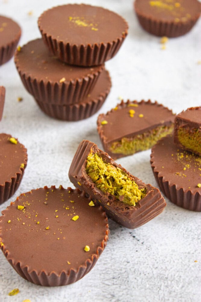 Chocolate cups filled with a yellowish nut mixture, some whole and some cut open, are arranged on a light textured surface.
