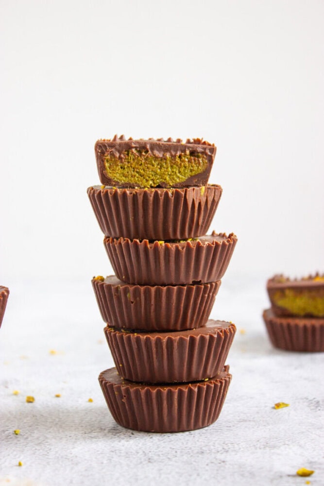 A stack of five chocolate cups with ridged edges, the top cup sliced to reveal a green filling. There are more chocolate cups blurred in the background.