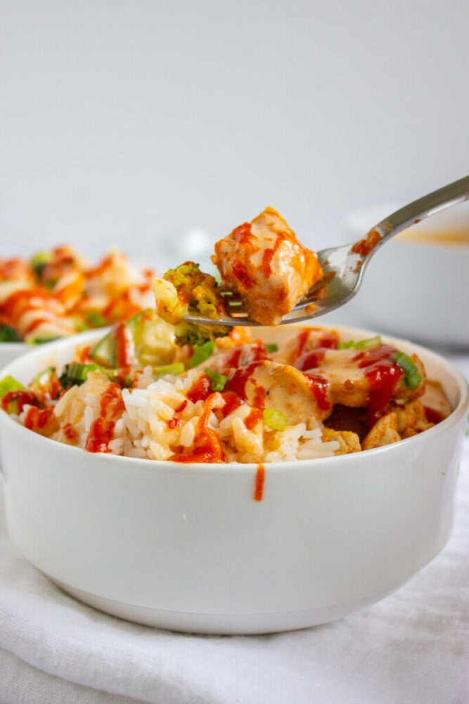 A bowl of white rice topped with vegetables, tofu, and red sauce, with a fork lifting a bite-sized portion above the bowl.