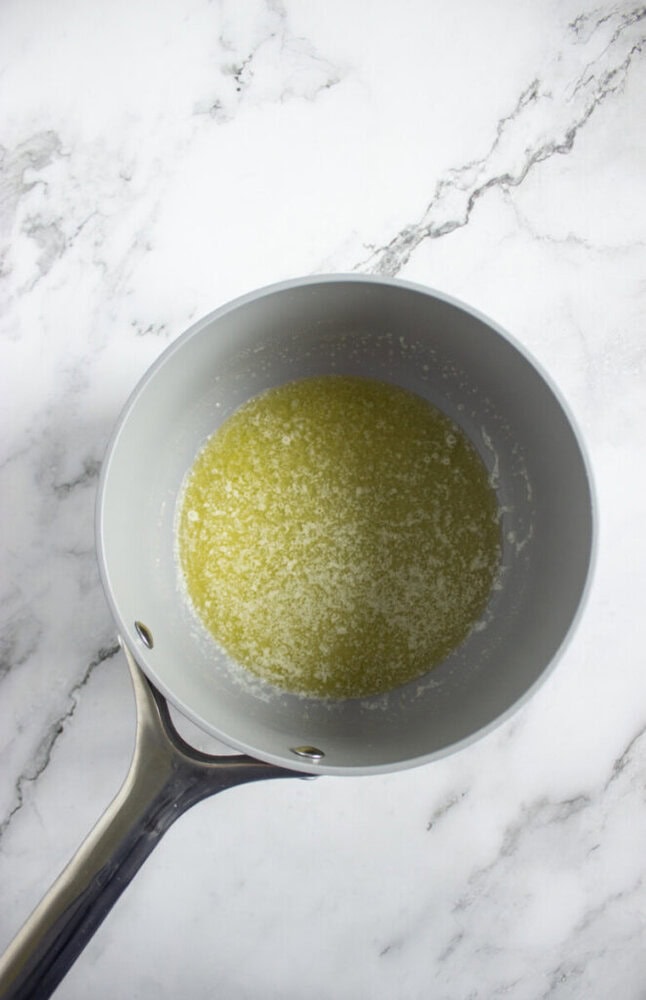 A saucepan with melted butter sits on a white marble surface.