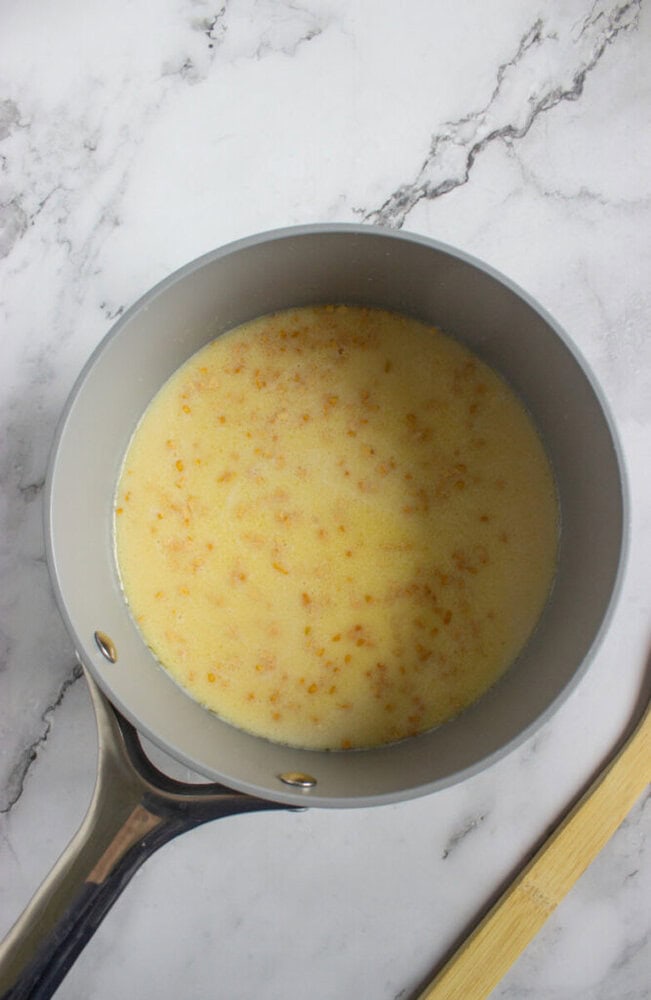 A saucepan with butter and lightly browned bits on the surface, sitting on a marble countertop next to a wooden spoon.