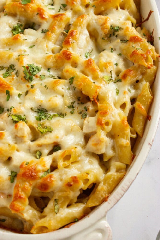 Baked pasta topped with melted cheese and garnished with chopped herbs in a white casserole dish.
