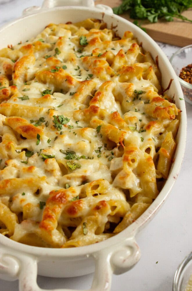 Baked pasta casserole topped with melted cheese and chopped herbs in a white oval dish.