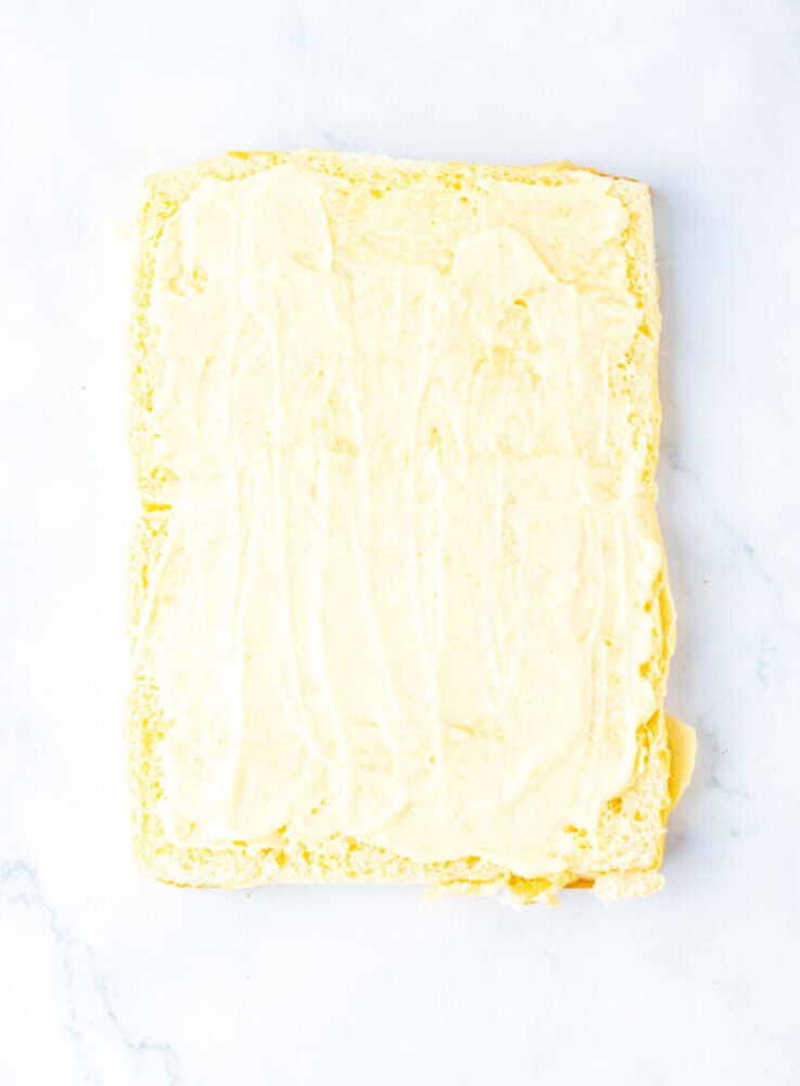 A rectangular sheet cake with a layer of yellow frosting spread evenly on top, placed on a white marble surface.