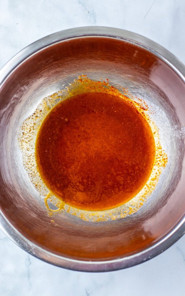 A stainless steel mixing bowl containing a reddish-brown liquid mixture sits on a white marble surface.