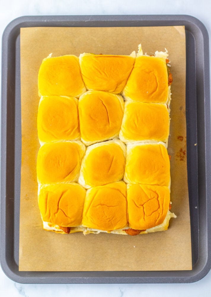 A tray of twelve golden-brown slider buns on a sheet of parchment paper.