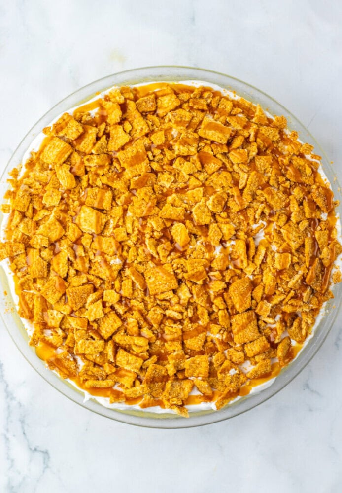 A round pie topped with a thick layer of crushed golden cereal pieces on a white marble surface.