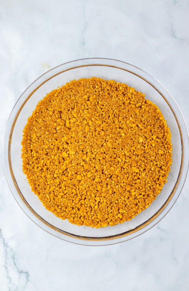 A glass bowl filled with a layer of finely crushed graham cracker crumbs on a white marble surface.
