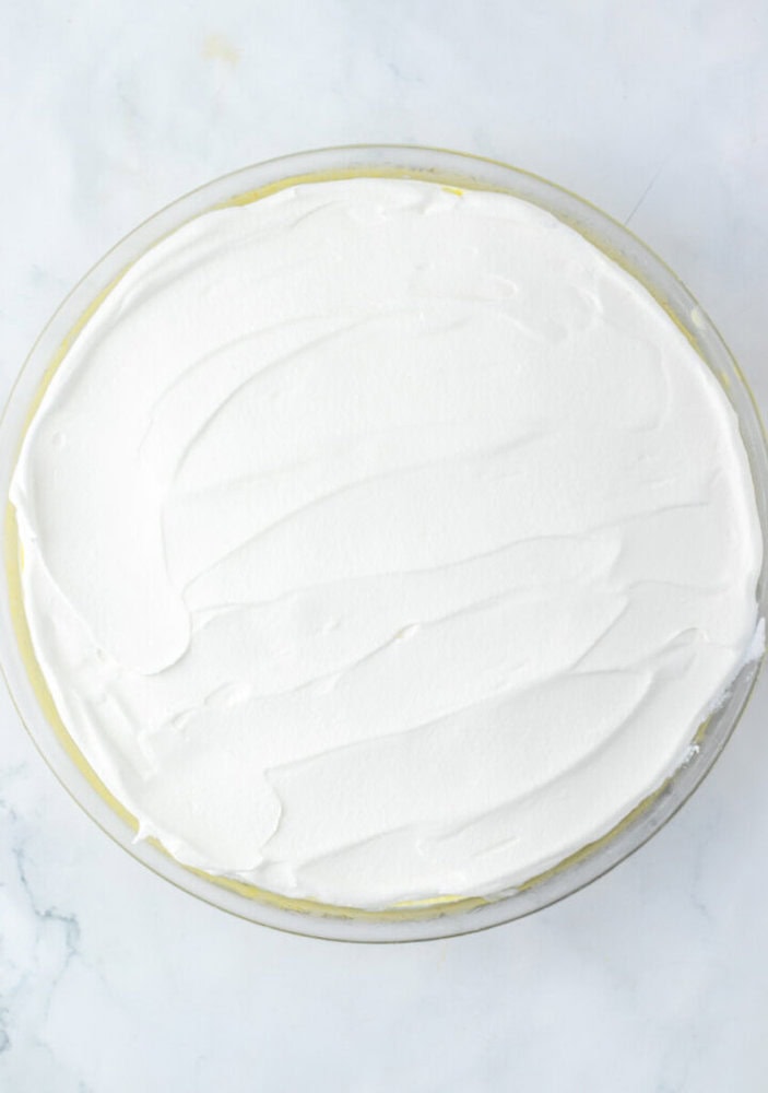 A round pie topped with a smooth, even layer of whipped cream, displayed on a white marble surface.