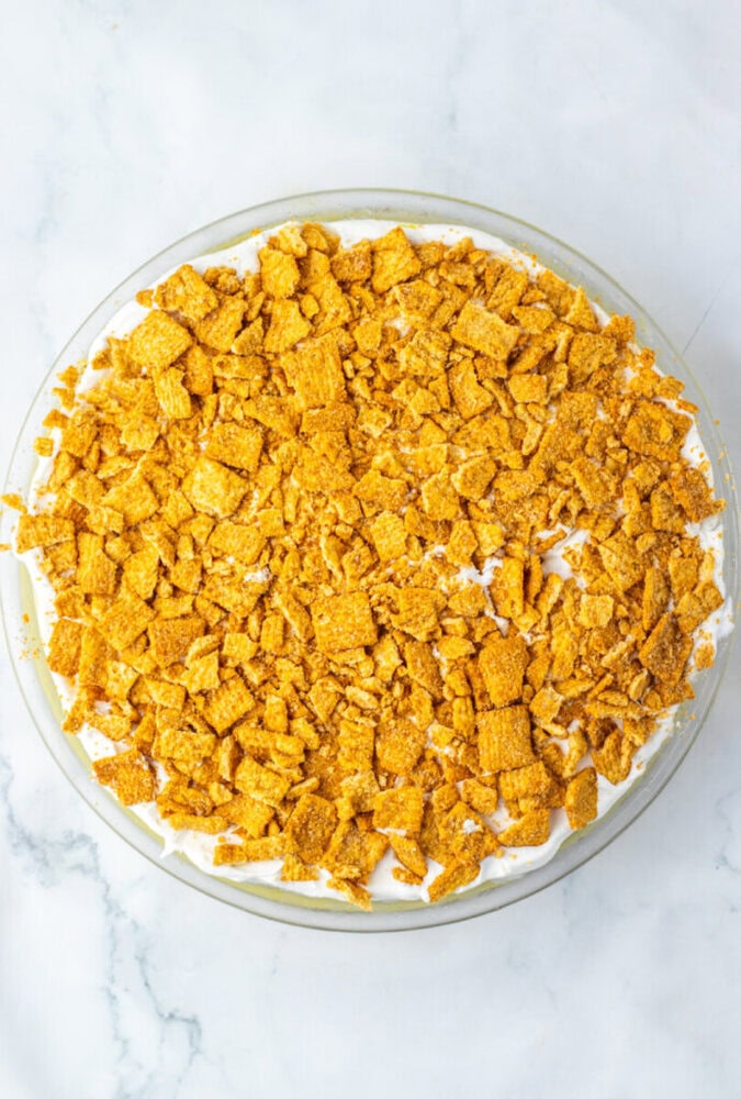 A round pie topped with a thick layer of crushed cereal pieces on a white marble surface.