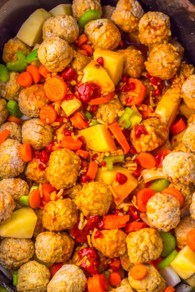 Meatballs, chopped carrots, celery, and potato chunks mixed with sauce and seasonings in a large pot, ready for cooking.