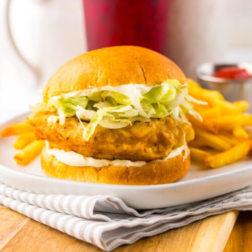 A fried chicken sandwich with lettuce and mayonnaise on a bun, served with French fries and a small cup of ketchup on the side.
