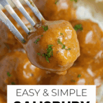 A fork holds a saucy meatball over a plate of Salisbury Steak Meatballs with brown gravy and herbs, perfect for Crockpot Salisbury Steak lovers.