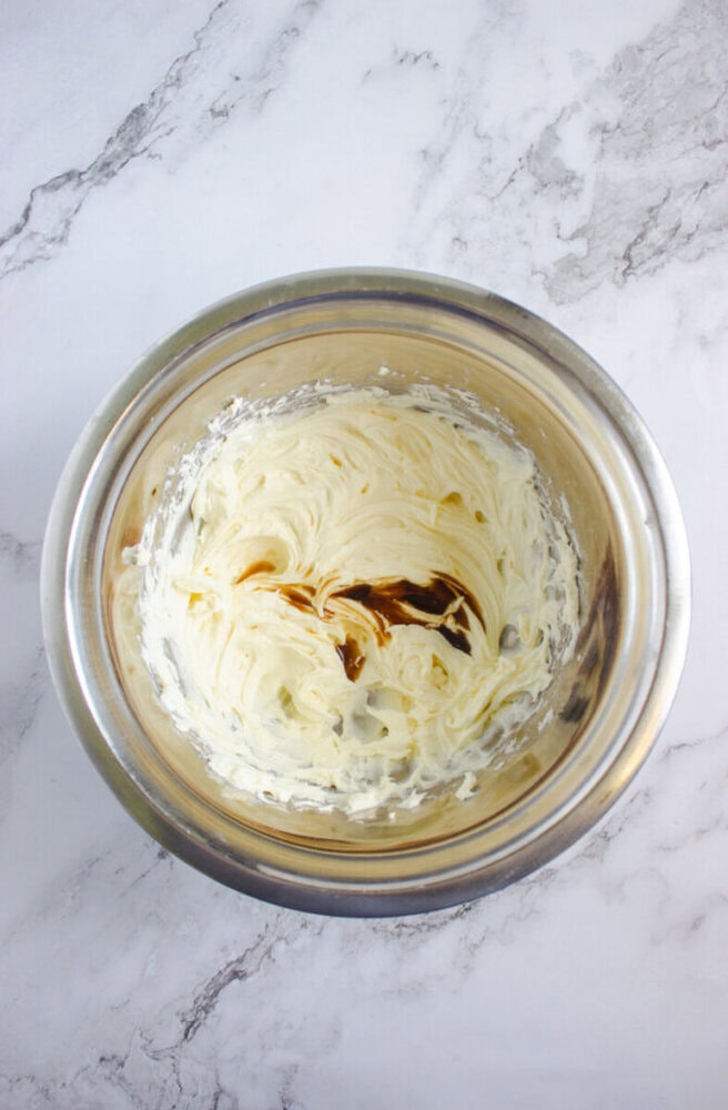 A metal mixing bowl containing creamed butter and sugar with vanilla extract added, set on a marble countertop.