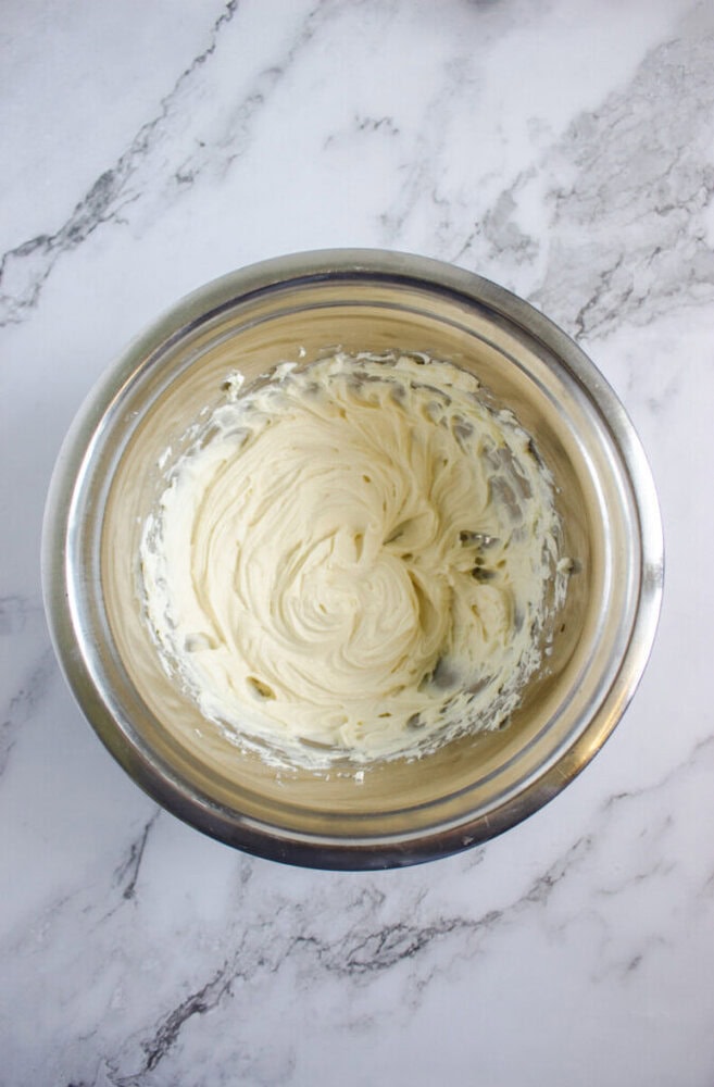A metal mixing bowl filled with creamy, whipped mixture sits on a white marble countertop.