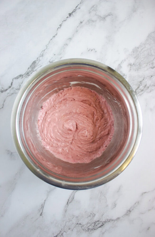 A stainless steel bowl filled with pink batter sits on a white marbled countertop.