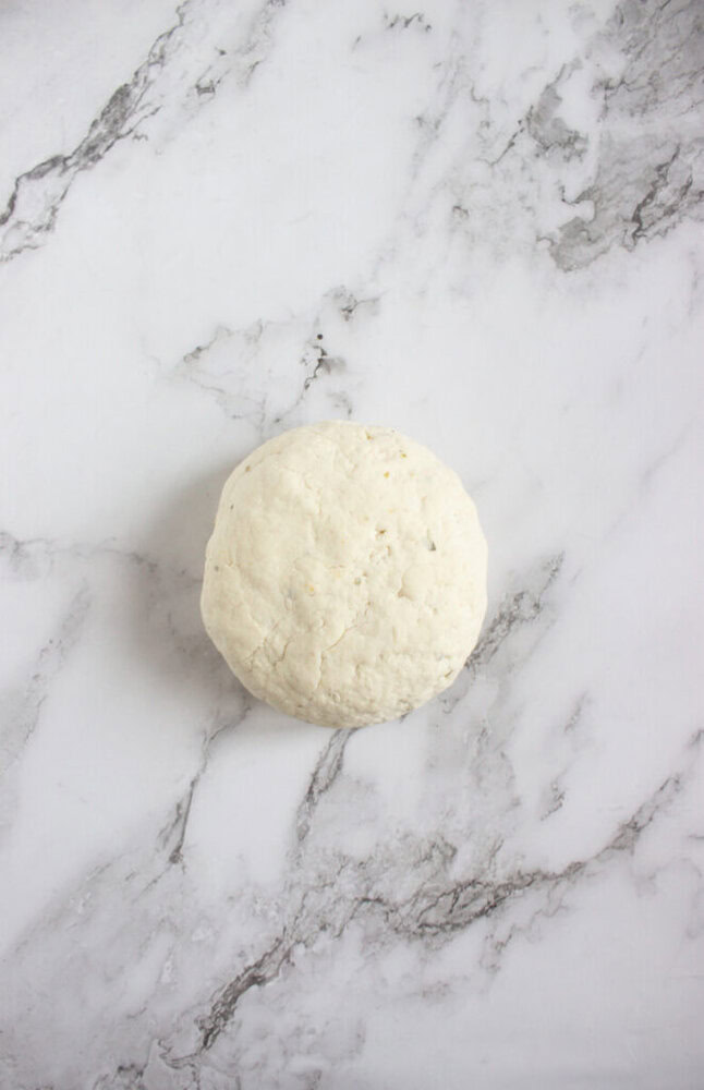 A ball of raw dough rests on a light gray marble surface.