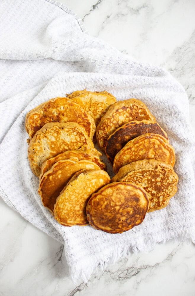 A plate with a variety of golden-brown pancakes arranged in a circle on a white cloth, set on a marble surface.