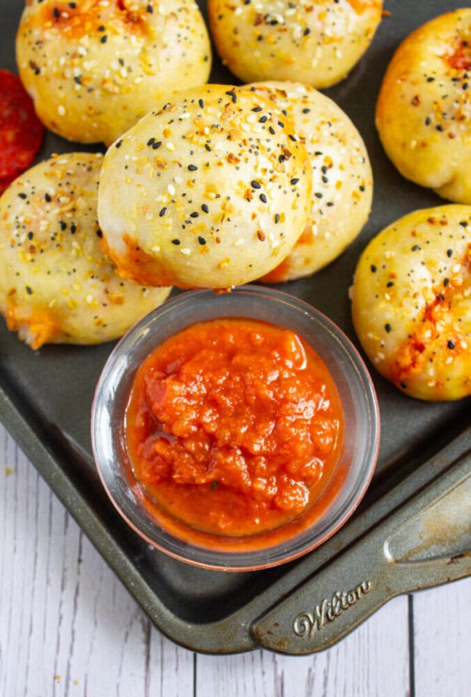 A tray of baked bread bites topped with seasoning is shown next to a small bowl of marinara sauce for dipping.