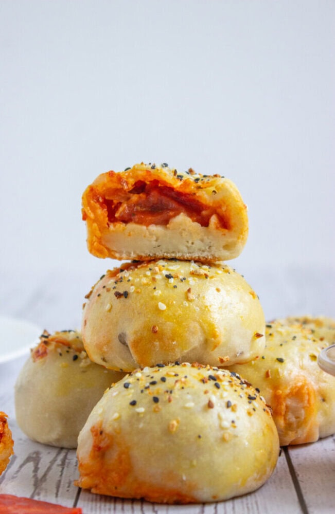 A stack of baked pizza rolls topped with seasoning, with the top roll cut open to show a tomato and cheese filling.