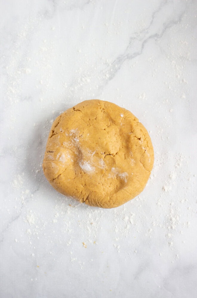 A round ball of raw dough sits on a lightly floured marble surface.