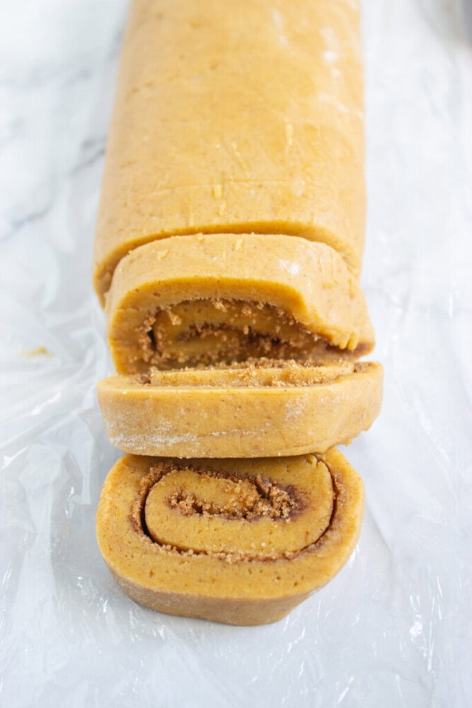 A rolled log of cinnamon dough with two slices cut, showing swirls of cinnamon filling on a white surface.