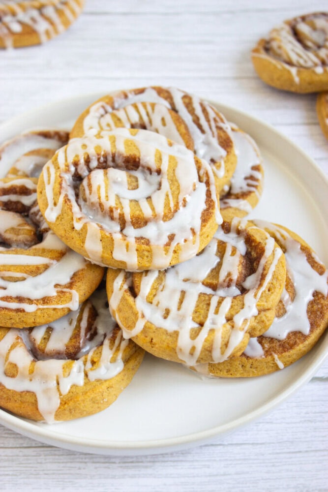 A plate of cinnamon rolls topped with white icing is placed on a light-colored surface.