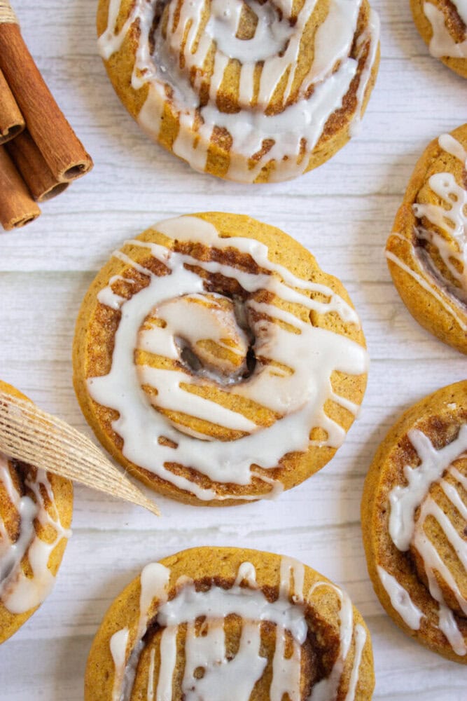 Overhead view of iced cinnamon rolls on a light wooden surface, with a bundle of cinnamon sticks nearby.
