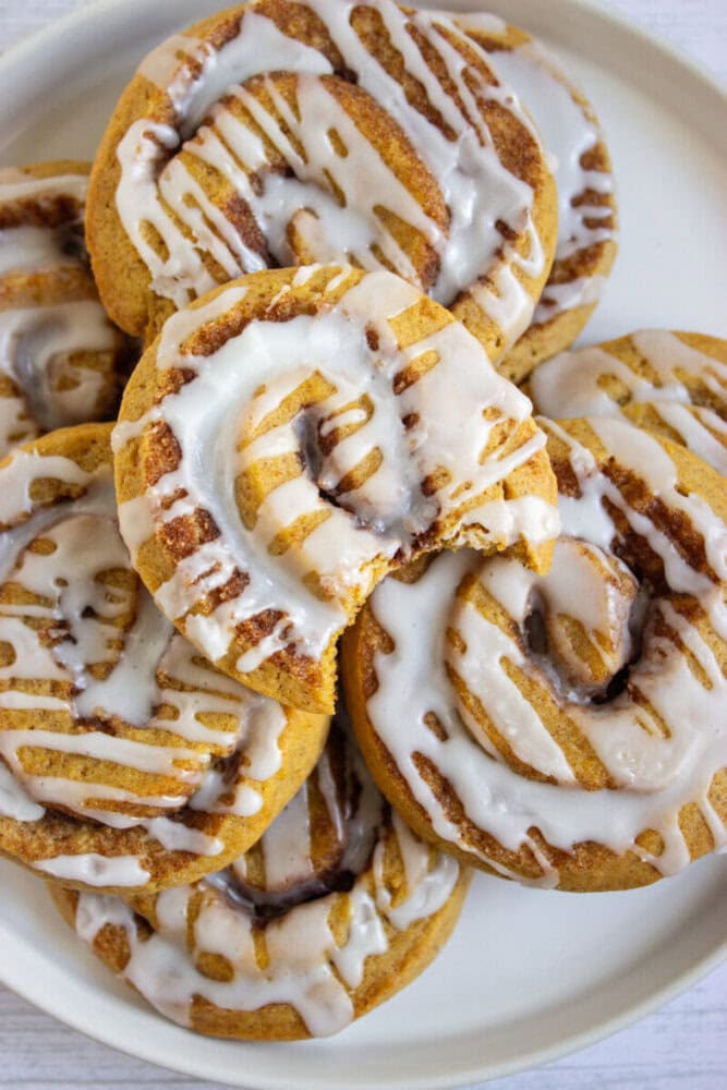 A plate of cinnamon rolls topped with white icing, with one roll showing a bite taken out of it.