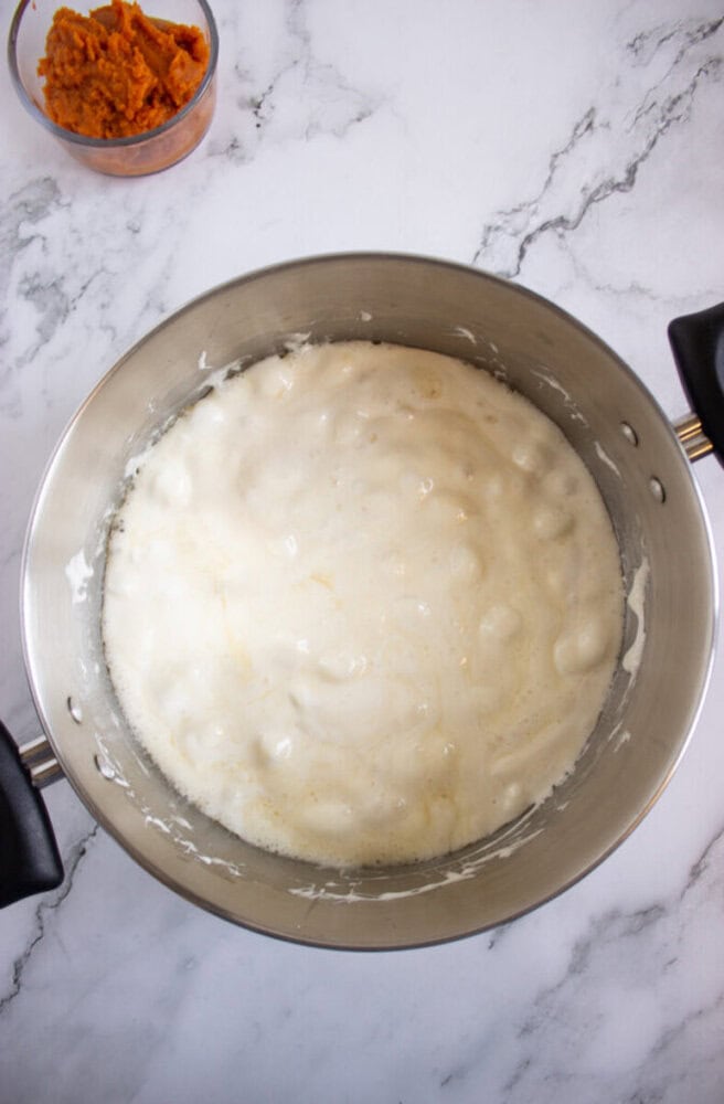 A stainless steel pot with melted marshmallows sits on a marble countertop; a small bowl of orange sweet potato mash is visible in the corner.