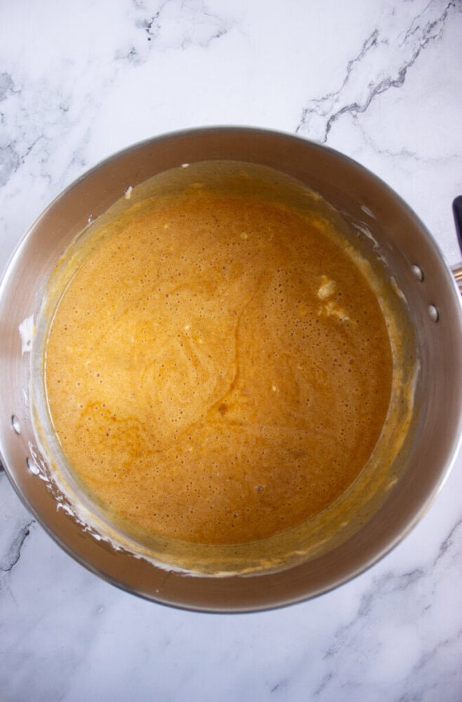 A metal mixing bowl containing a smooth, light brown batter sits on a white marble surface.