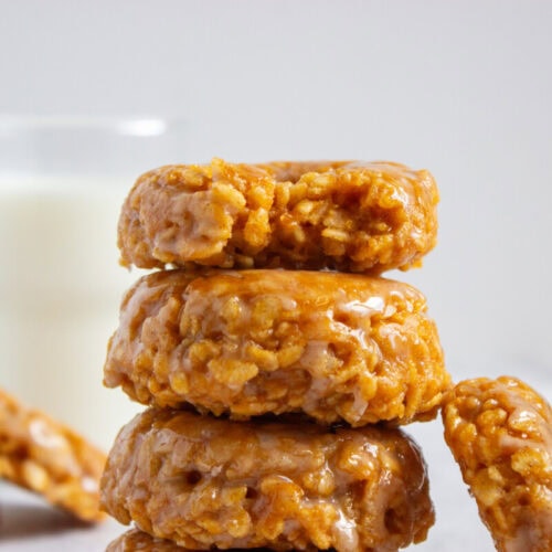 A stack of four glazed peanut butter oat cookies with a glass of milk in the background.