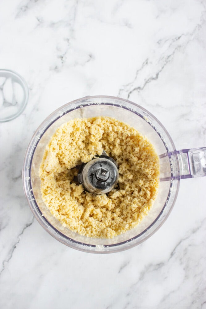 A food processor bowl filled with finely ground crumbs sits on a white marble countertop.