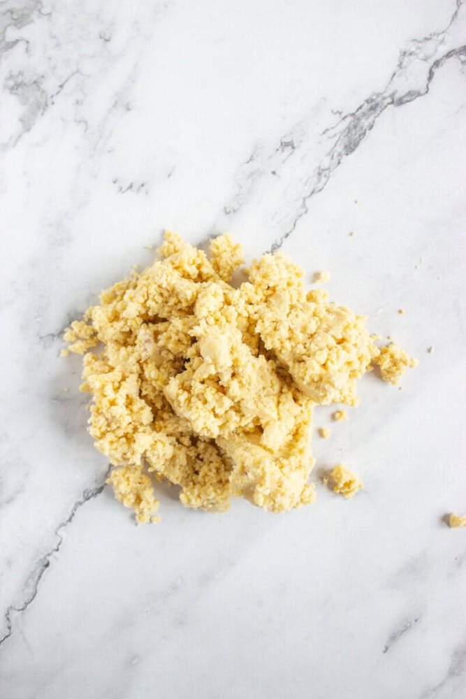 A pile of crumbly, pale yellow dough mixture on a white marble surface.