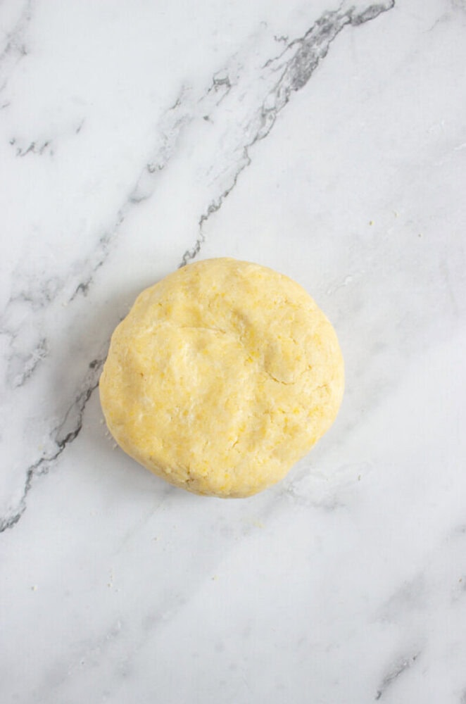 A round ball of raw dough sits on a white marble surface.