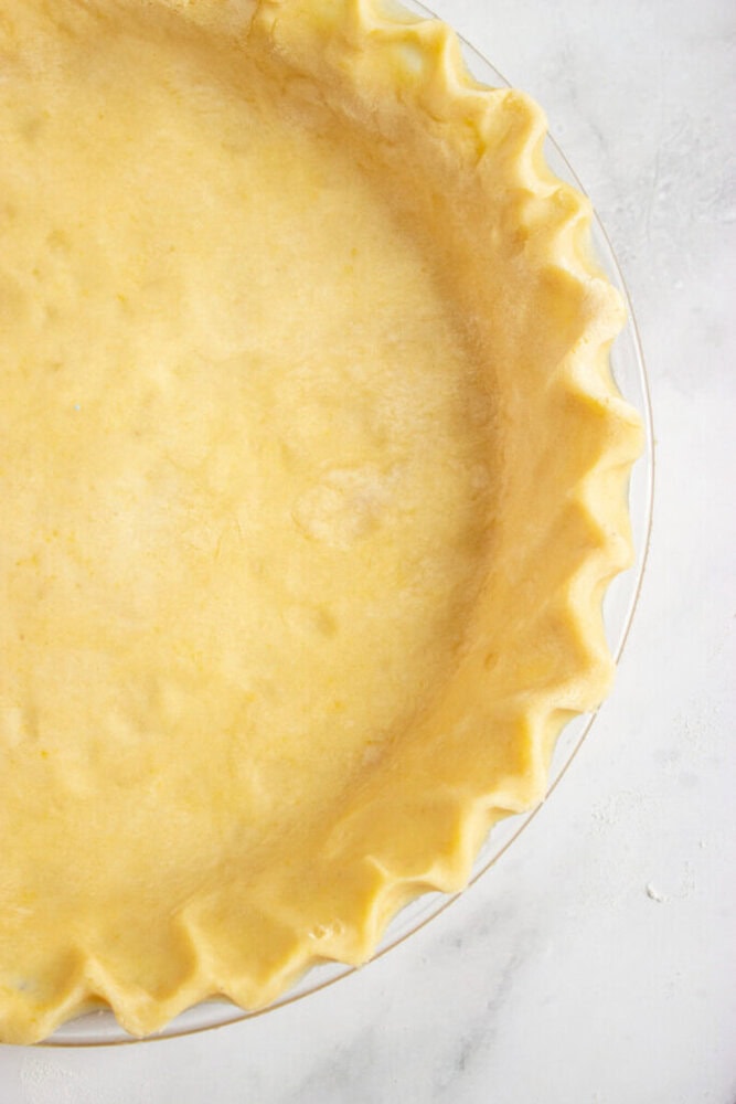 Unbaked pie crust with fluted edges in a glass pie dish on a white surface.