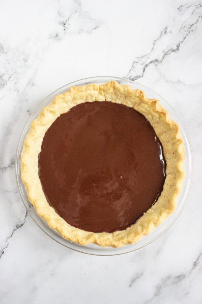 A chocolate pie with a golden, flaky crust sits on a white marble surface.