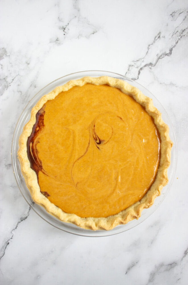 A baked pumpkin pie with a golden crust sits on a white marble surface.