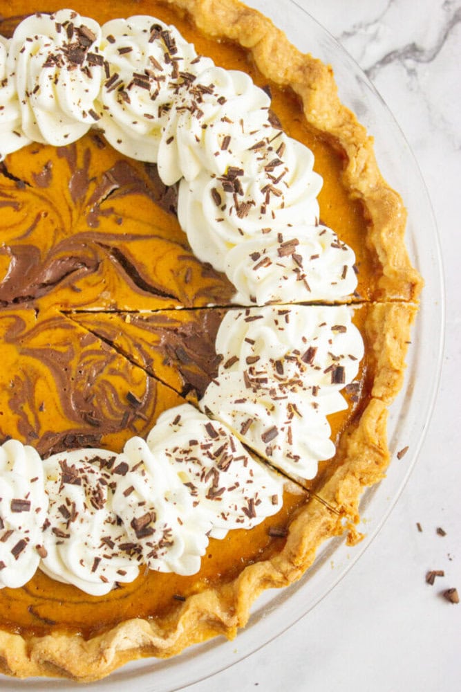 Pumpkin pie with a marbled chocolate swirl, topped with piped whipped cream and chocolate shavings, with two slices cut.