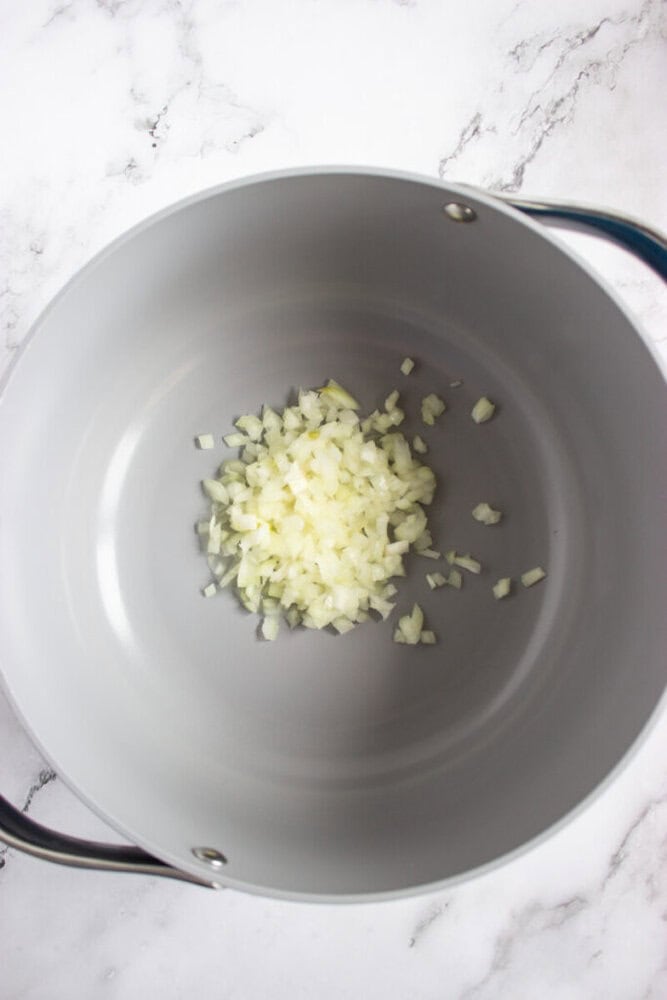 Chopped onions in the center of a large, empty gray pot on a white marble surface.