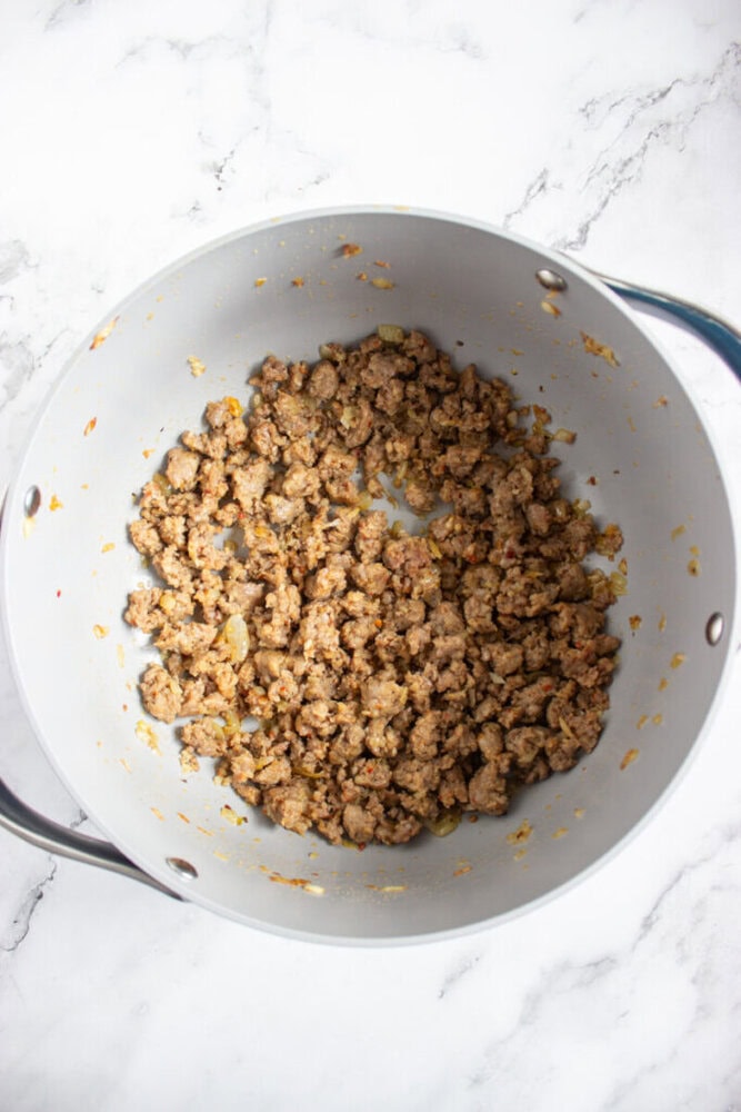 Cooked ground meat with seasonings and small onion pieces in a large pot, shown from above on a white marble surface.